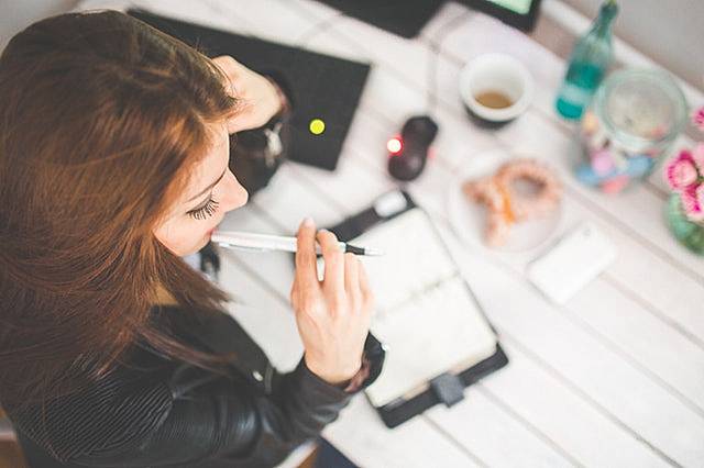 ペンを持ちながらデスクで考え事をしている女性の写真